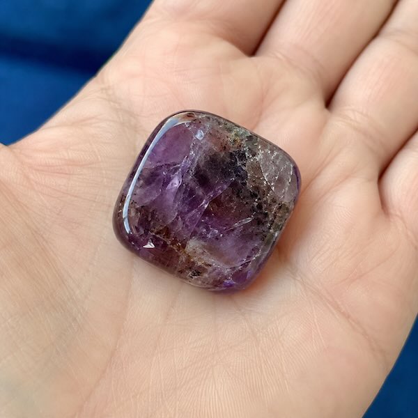Auralite 23 lommesten med smukke lilla nuancer og naturlige mineralindeslutninger. Poleret krystal fotograferet tæt på i hånden.