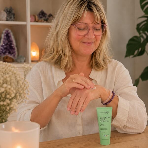 Kvinde sm&oslash;rer Born to Bio Aloe Vera h&aring;ndcreme p&aring; h&aelig;nderne i hyggelige og naturlige omgivelser med krystaller og wellness stemning.