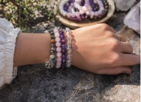 Krystalarmb�nd med ametyst, rosenkvarts og bjergkrystal p� h�ndled i naturligt lys og rolige jordn�re omgivelser.