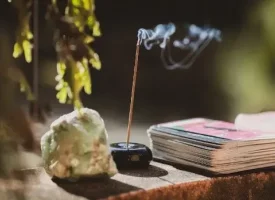 Et billede af en rgelsesholder med en rgelsespind og en krystal og nogle tarotkort