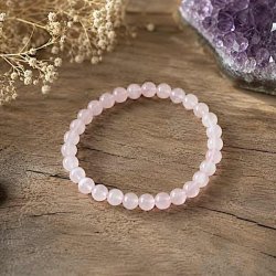 Rosenkvarts krystalarmb�nd med 6 mm perler p� naturlig tr�overflade omgivet af dekorative elementer i bl�dt dagslys.