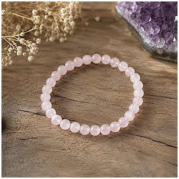 Rosenkvarts krystalarmb�nd med 6 mm perler p� naturlig tr�overflade omgivet af dekorative elementer i bl�dt dagslys.