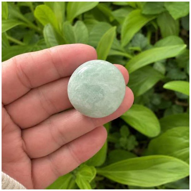 Poleret mintgr�n amazonit lommesten holdt i h�nden med gr�nne planter i baggrunden