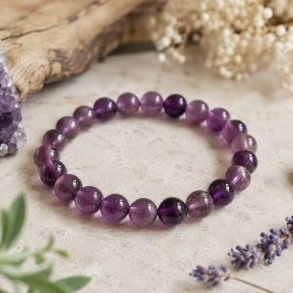 Ametyst armb�nd med 8 mm perler fotograferet p� en lys natursten i bl�dt dagslys med naturlig baggrund.