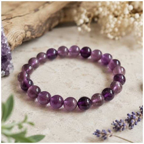 Ametyst armb�nd med 8 mm perler fotograferet p� en lys natursten i bl�dt dagslys med naturlig baggrund.
