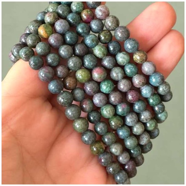 Rubin-safir-stenperler i gr�nne, bl�lige og violette nuancer vist t�t p� i h�nden.