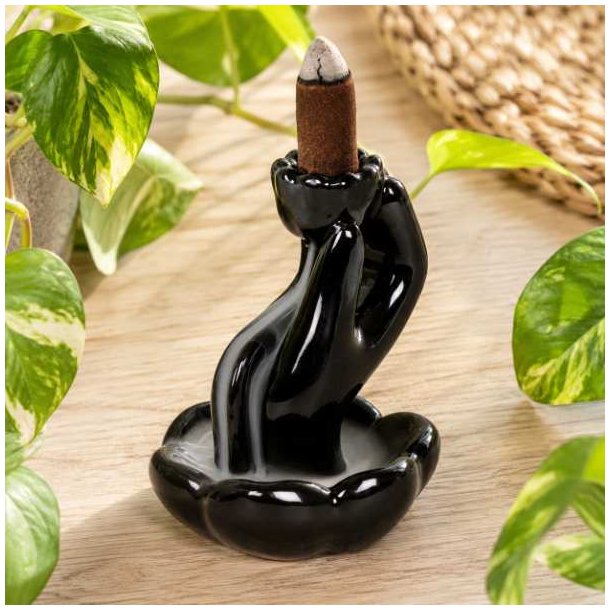 Sort backflow r�gelsesholder i glaseret keramik med r�gelseskegle omgivet af gr�nne planter.