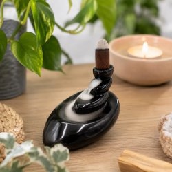 Backflow r�gelsesholder In Balance i sort glaseret keramik med vandfaldseffekt p� lyst tr�bord omgivet af gr�nne planter og stearinlys.