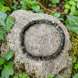 Elastisk unisex armb�nd med h�matit og lavasten placeret p� en sten omgivet af gr�nne planter