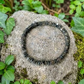 Elastisk unisex armb�nd med h�matit og lavasten placeret p� en sten omgivet af gr�nne planter