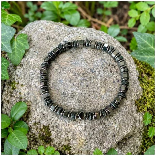 Elastisk unisex armb�nd med h�matit og lavasten placeret p� en sten omgivet af gr�nne planter