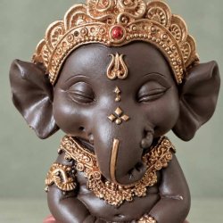 T�t p� n�rbillede af m�rkebrun Ganesha figur med fokus p� elefantgudens ansigt, snabel og detaljerede guldkrone med r�d plet.