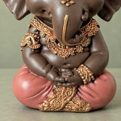 N�rbillede af m�rkebrun Ganesha figur i meditativ stilling, der viser detaljerne i den rosa kl�dedragt og elefantgudens h�nder.