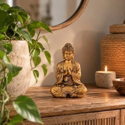Siddende Buddha statue i polyresin med bedende h�nder, stylet i et moderne hjem foran et spejl p� en tr�sk�nk.