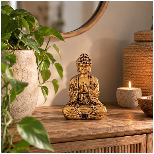 Siddende Buddha statue i polyresin med bedende h�nder, stylet i et moderne hjem foran et spejl p� en tr�sk�nk.