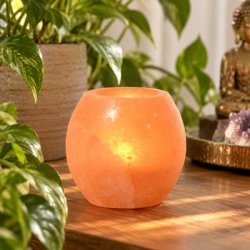 H�ndpoleret Himalaya salt fyrfadsstage i varm rosa-orange saltsten p� tr�bord omgivet af gr�nne planter.