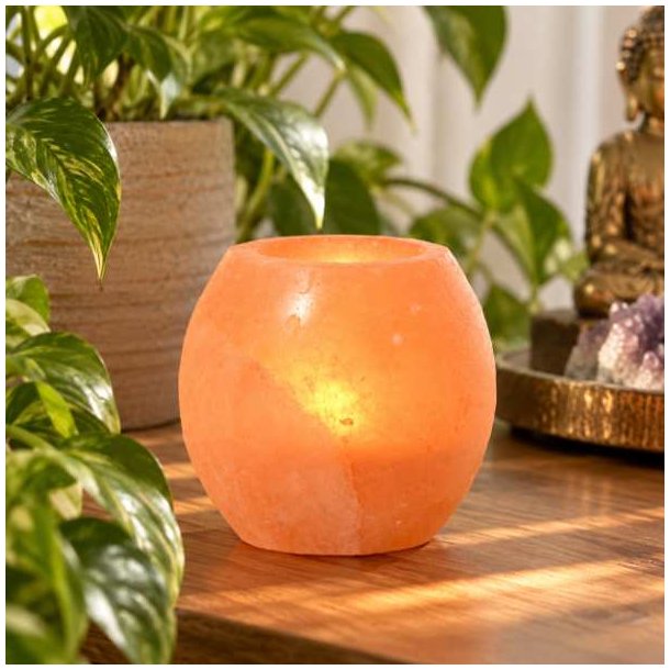 H�ndpoleret Himalaya salt fyrfadsstage i varm rosa-orange saltsten p� tr�bord omgivet af gr�nne planter.