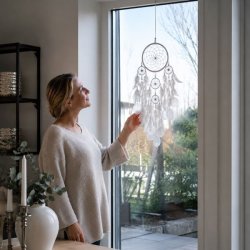 Hvid h�ndlavet dr�mmefanger med Capiz-skaller og hvide fjer h�ngende i vindue med model som illustrerer st�rrelsen.