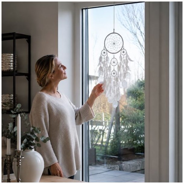 Hvid h�ndlavet dr�mmefanger med Capiz-skaller og hvide fjer h�ngende i vindue med model som illustrerer st�rrelsen.