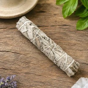Hvid salvie smudge stick 18 cm p� naturbord omgivet af gr�nne planter &ndash; h�ndbundet salviebundt til smudging og energirensning.