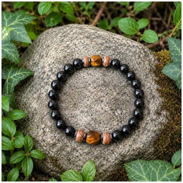 Elastisk unisex armb�nd med sort onyx, gyldent tiger�je, h�matit og tr� placeret p� en natursten omgivet af gr�nne planter