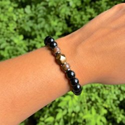 Elastisk stenarmb�nd med sort onyx, tiger�je, h�matit og tr� b�ret p� h�ndled foran gr�nne planter