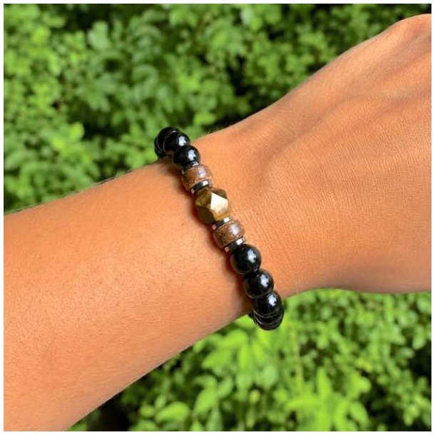 Elastisk stenarmb�nd med sort onyx, tiger�je, h�matit og tr� b�ret p� h�ndled foran gr�nne planter
