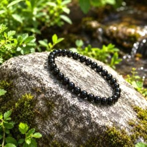Sort obsidian krystalarmb�nd 6 mm p� natursten omgivet af gr�nne planter &ndash; elastisk armb�nd med �gte vulkansk glas.