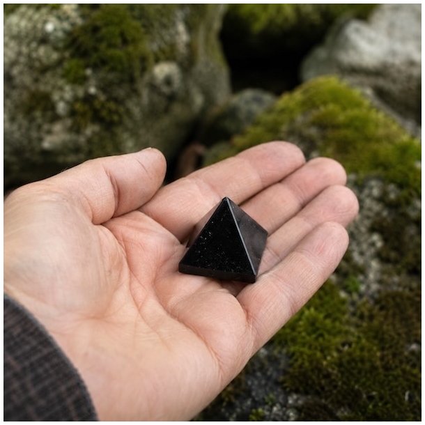 H�nd holder lille sort turmalin pyramide udend�rs i naturligt milj� med mos og sten