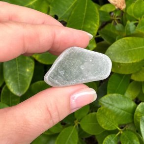N�rbillede af en tromlet Ulexit TV-sten holdt mellem fingrene med gr�nne planter i baggrunden. Naturlig Ulexit med silkeglinsende overflade.