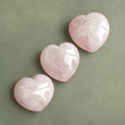 Tre buttede, lyser�de krystalhjerter af rosekvarts liggende p� en r�kke p� en d�mpet gr�n baggrund.